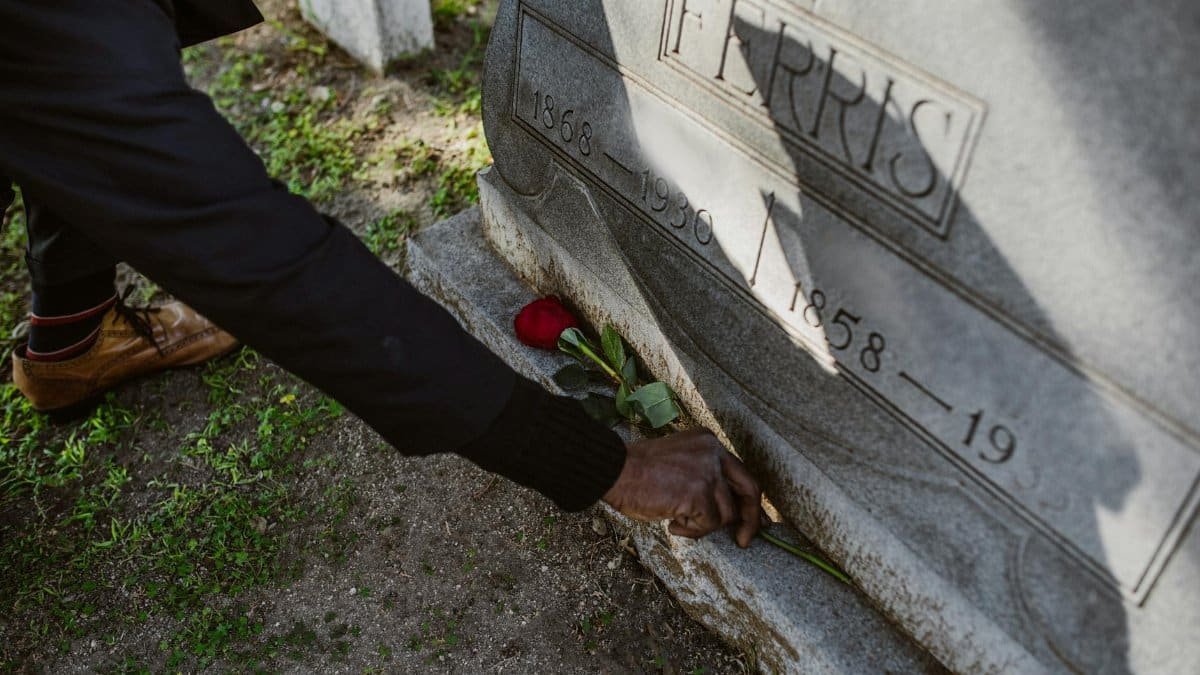 A man places a rose on a gravestone, symbolizing grief and reflection in a cemetery.