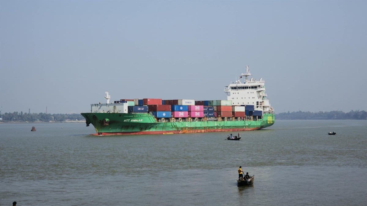 A colorful cargo ship carrying containers sails peacefully on a river, with small boats nearby.