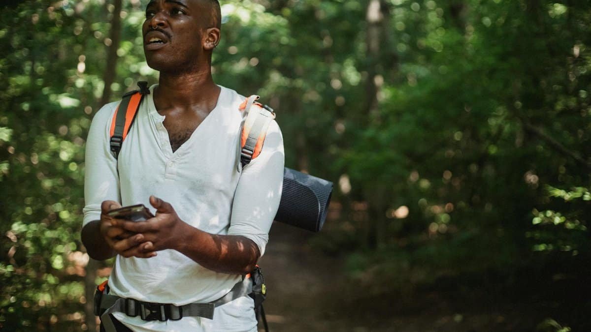 A hiker looks frustrated while using a smartphone to navigate in a dense forest.