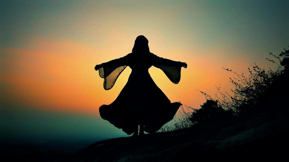 A dramatic silhouette of a woman in a dress, arms extended, against a vibrant sunset sky.