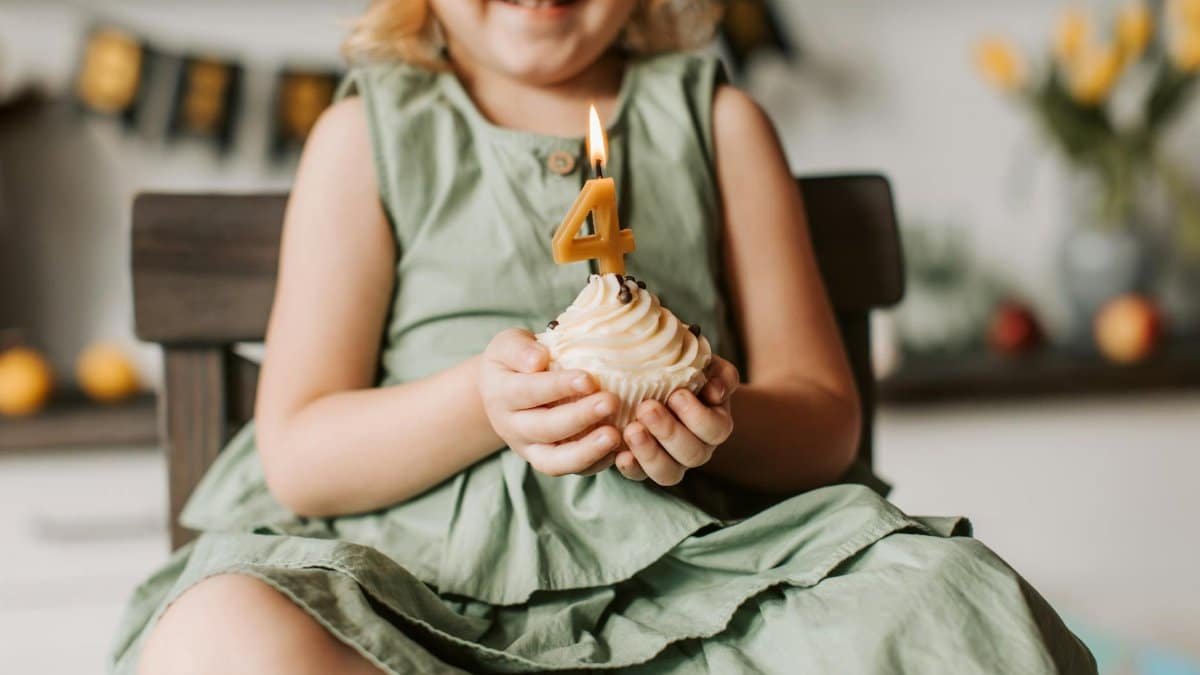 Happy child holding a cupcake with number four candle, celebrating a birthday indoors.