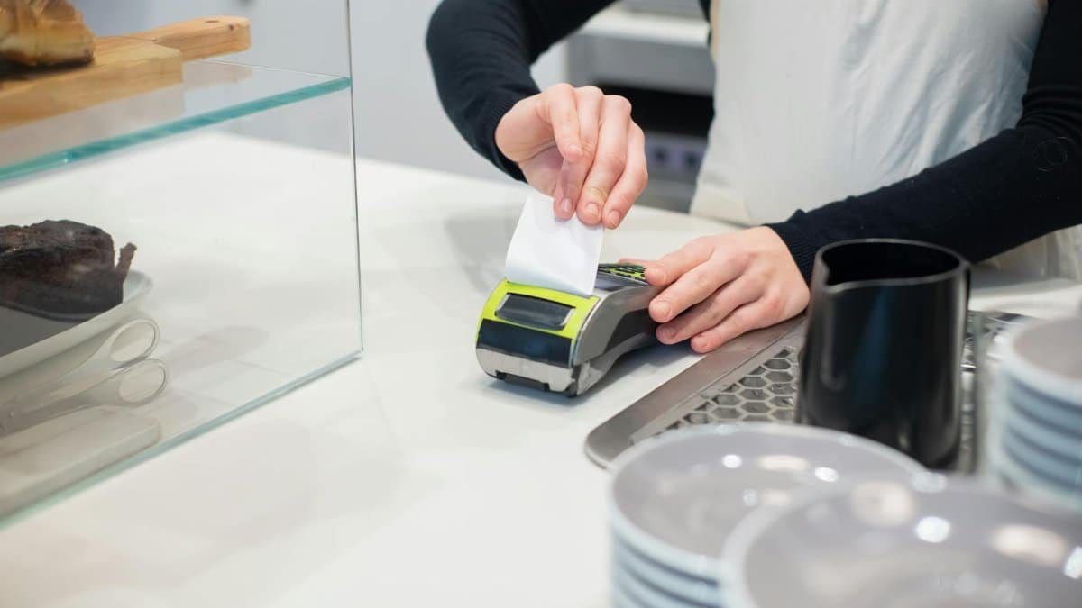 Close-up of a cashless transaction at a modern café counter with hands holding a receipt.