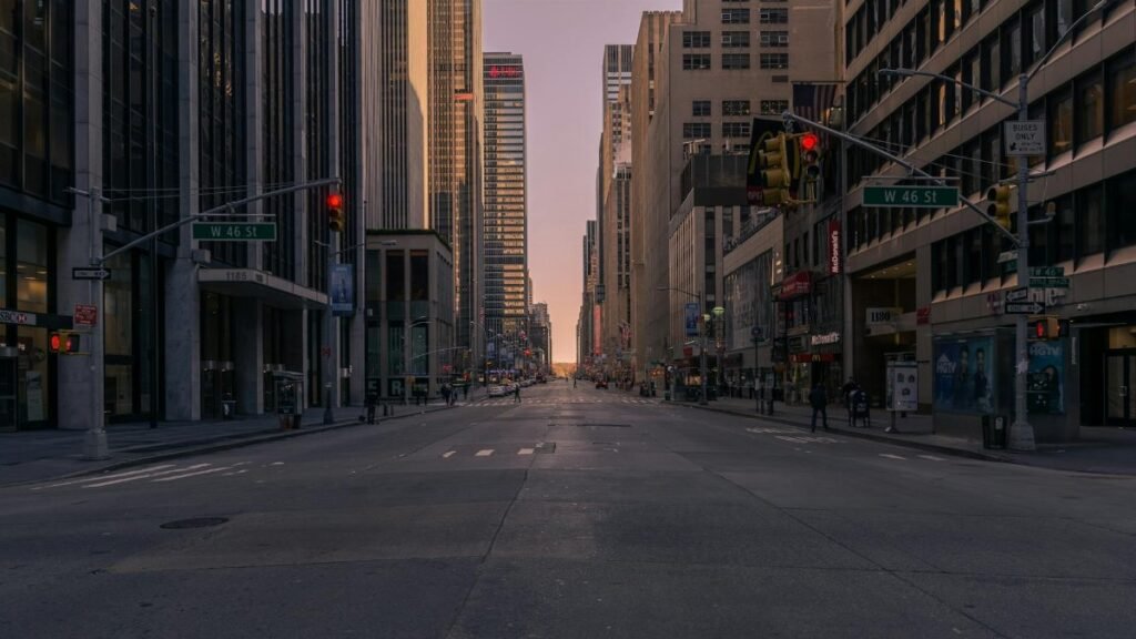 Empty New York City street at sunset with towering skyscrapers and soft glowing light.