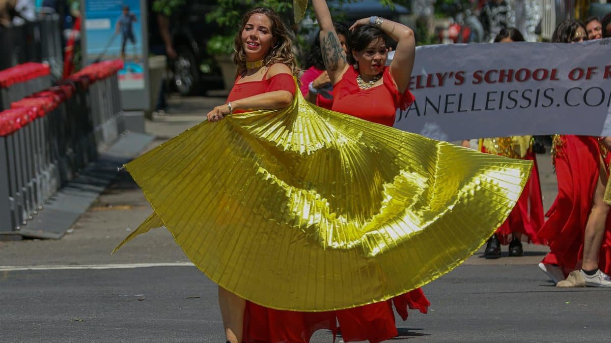 Performers in vibrant costumes dance in a lively street parade in New York City, capturing the spirit of cultural celebration.
