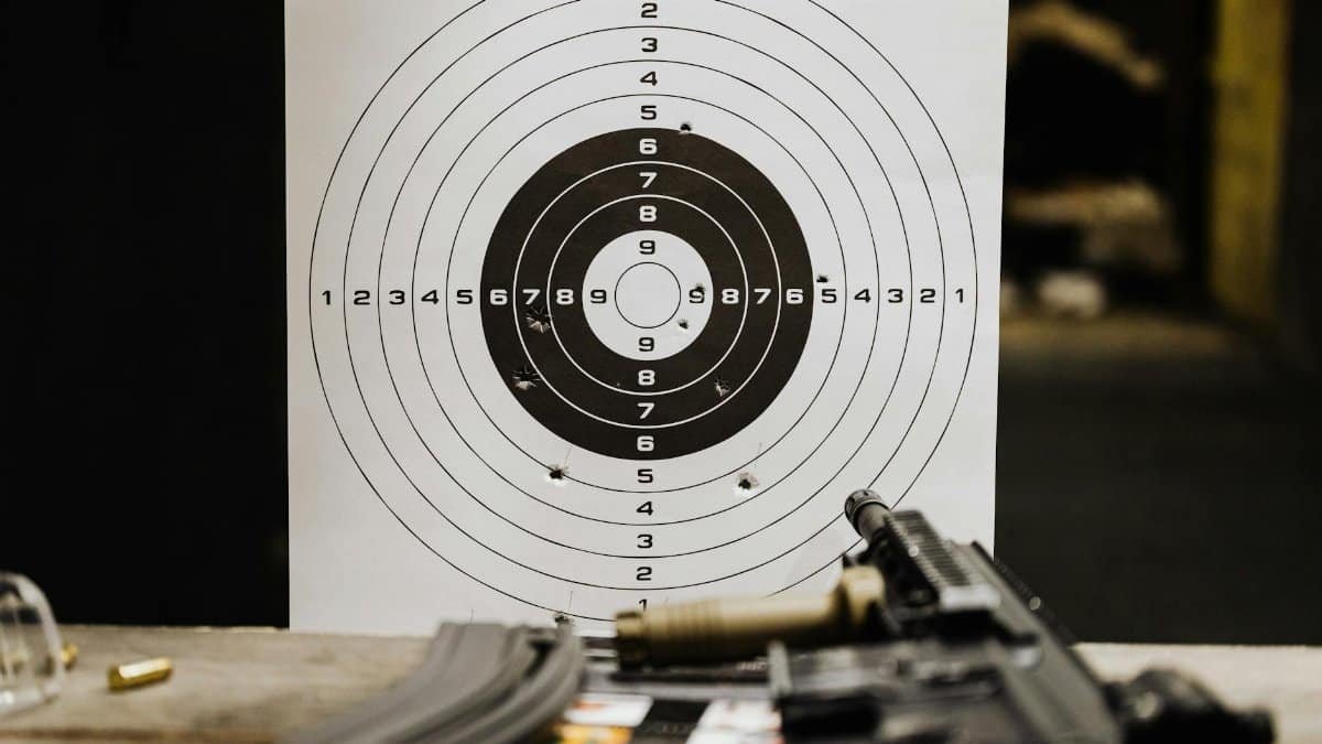 Close-up of a shooting target with bullet holes on a range table next to a rifle.
