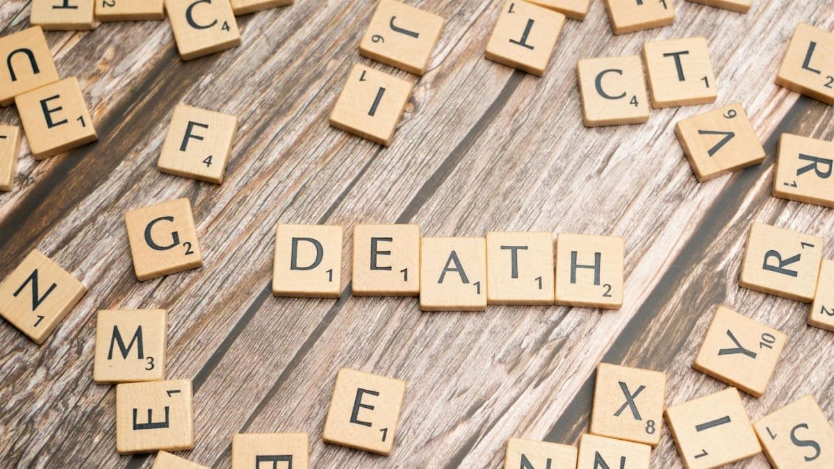 Wooden Scrabble tiles spelling 'Death' on a rustic surface, emphasizing themes of mortality.