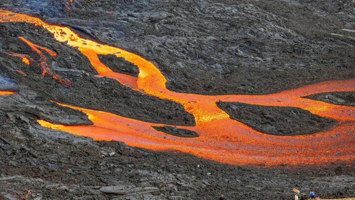 A vibrant lava flow captivating tourists in a dramatic volcanic landscape.