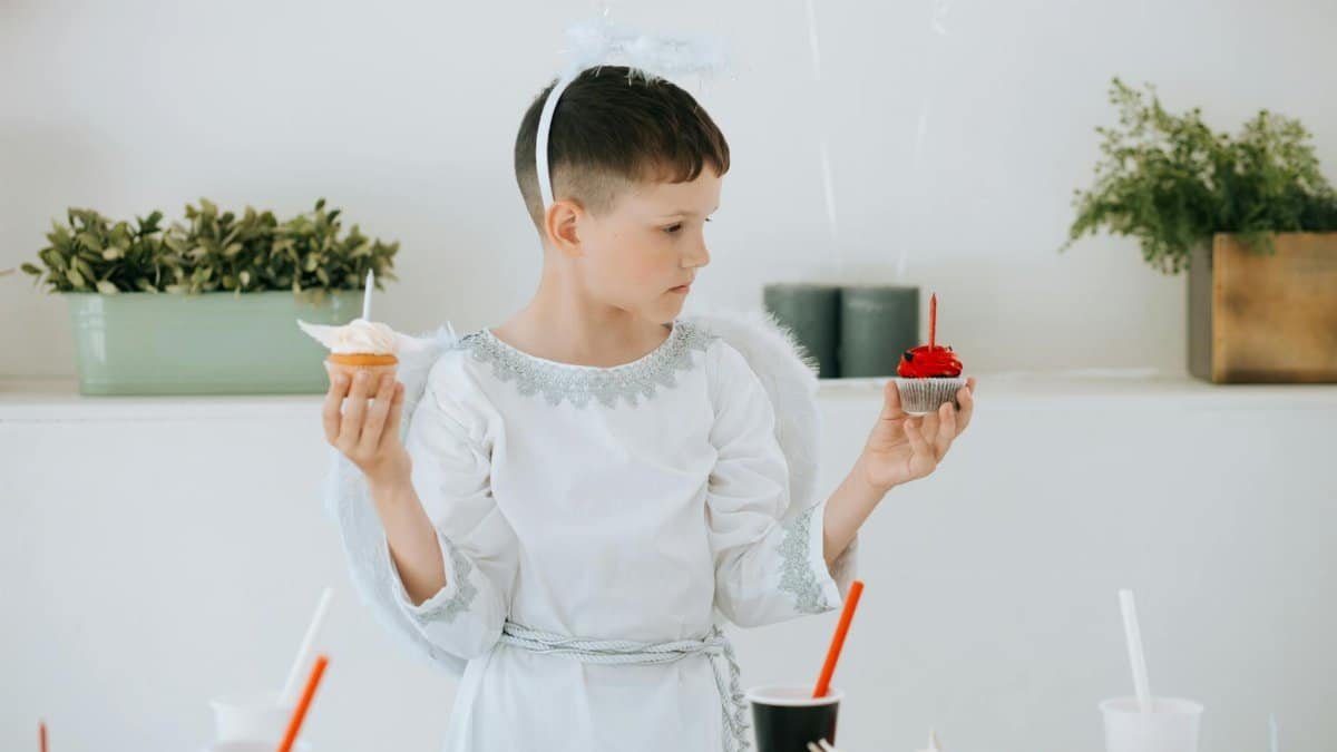 A child dressed as an angel holding cupcakes during a festive celebration.