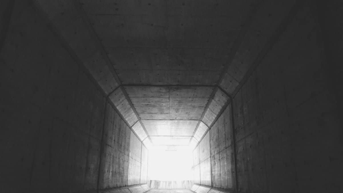 Black and white photo of a concrete tunnel with bright light at the end.