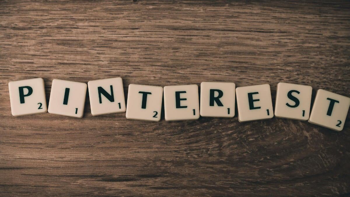 Scrabble tiles spelling Pinterest on a wooden background, symbolizing social media and creativity.