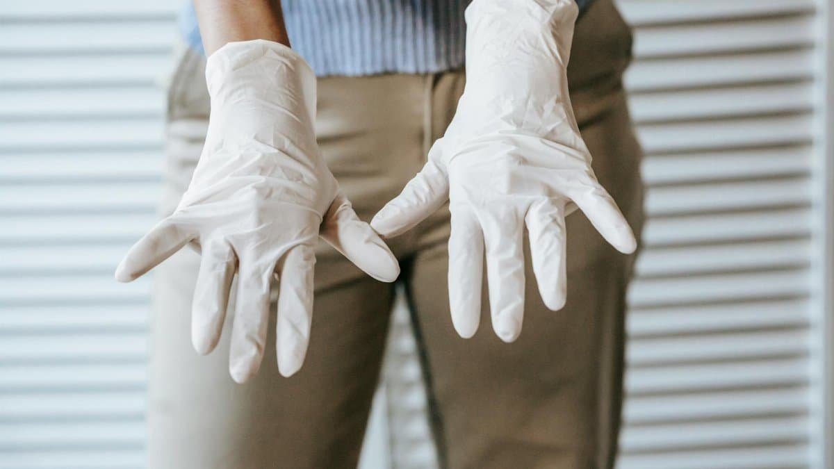 Close-up of a woman wearing white latex gloves showing hands forward as protection measure.