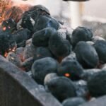 Sparks fly from burning charcoal on a barbecue grill, creating a hot and fiery atmosphere.