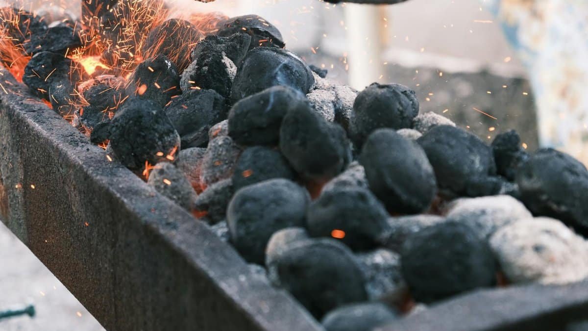 Sparks fly from burning charcoal on a barbecue grill, creating a hot and fiery atmosphere.