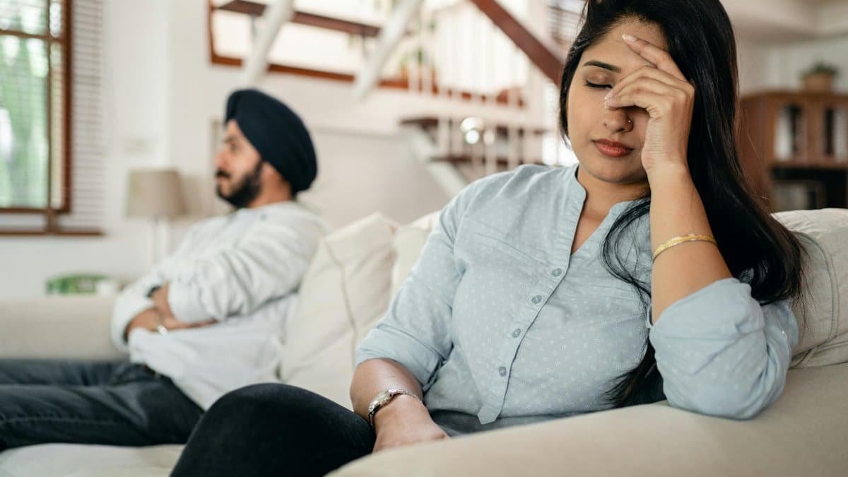 A young couple sitting on a couch indoors, showing signs of stress and frustration.