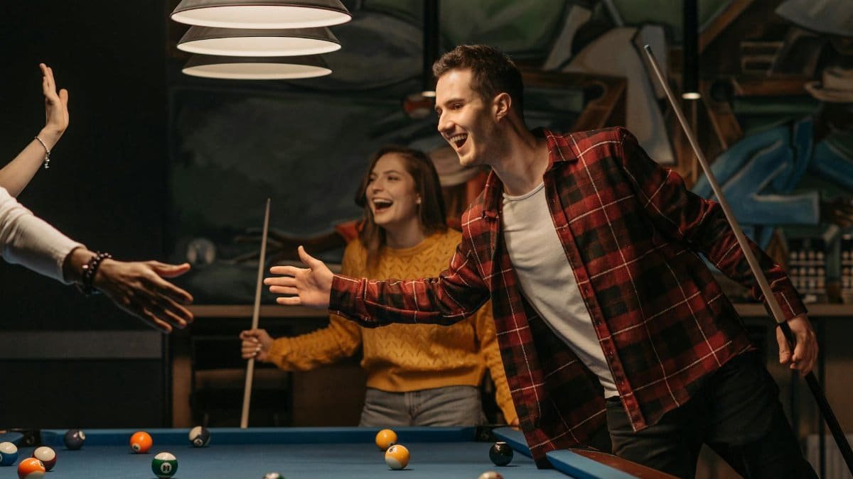 Two friends celebrate a successful billiards shot with a high-five indoors, youthful and vibrant.