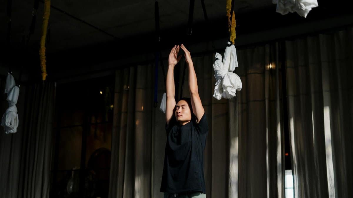 A man stretches during an indoor yoga session with aerial silks, promoting health and wellness.