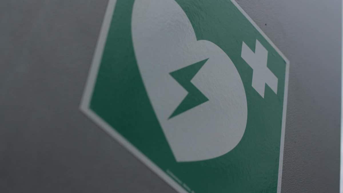 Green first aid sign featuring a broken heart and cross symbol for medical emergency awareness.