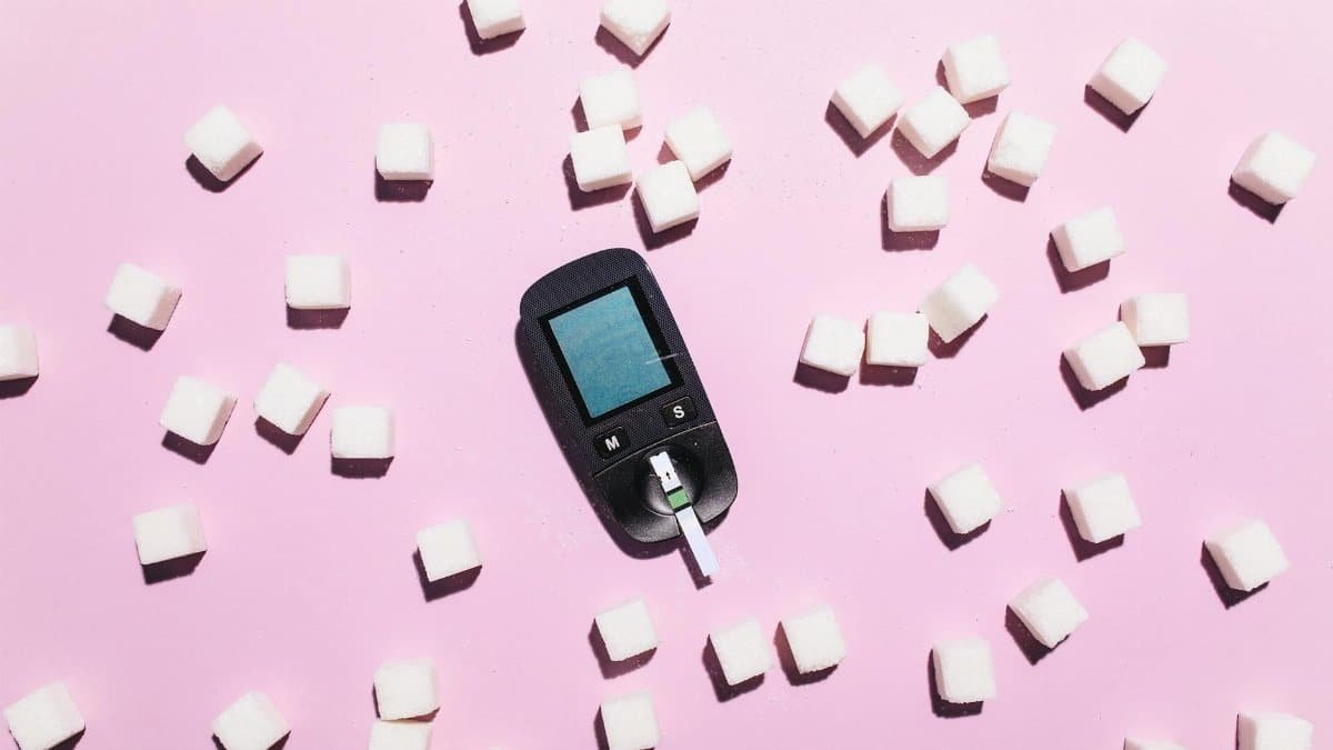 Blood glucose meter surrounded by sugar cubes on a pink background, highlighting diabetes awareness.