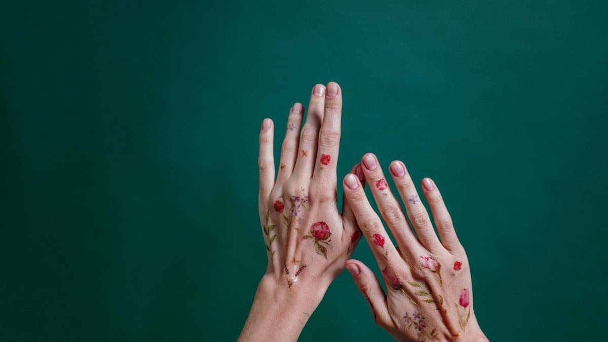Hands with floral temporary tattoos against a solid green background, showcasing body art and self-care.