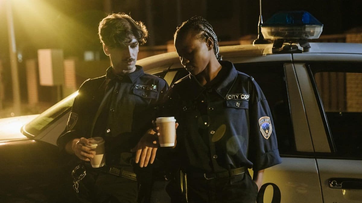 Two police officers enjoying a coffee break beside their patrol car during a night shift.
