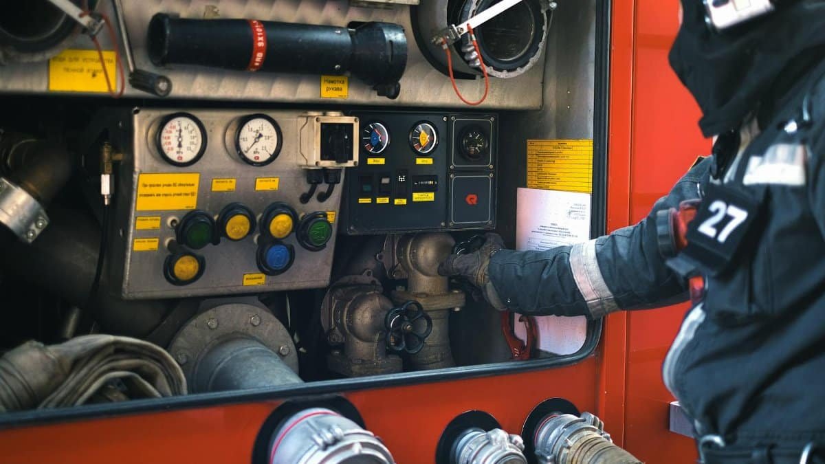 A firefighter in gear adjusting controls on a fire engine during an emergency response.