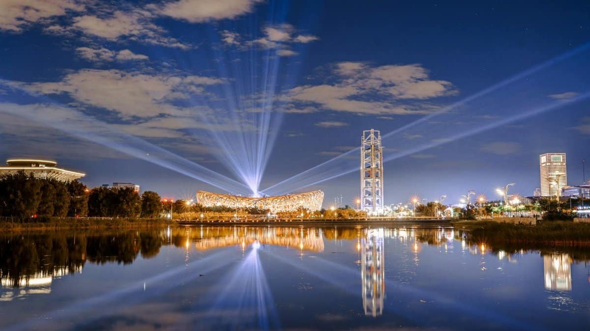 Stunning nightscape of Beijing's Olympic Bird's Nest Stadium reflecting in a calm lake, showcasing modern architecture under a starry sky.