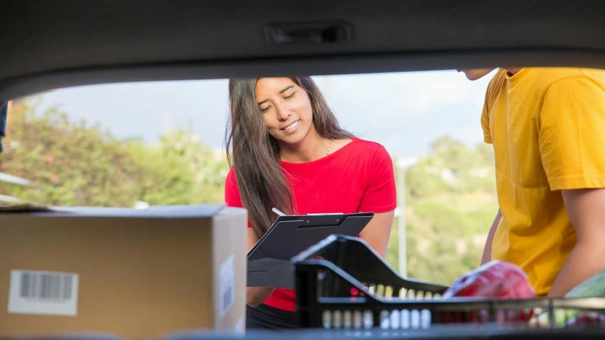 Smiling woman delivers packages from a car outdoors, enhancing customer experience.