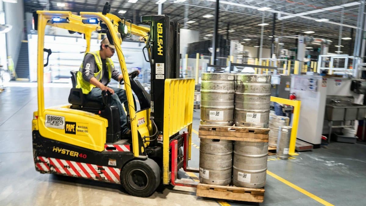 Forklift operator in warehouse moving beer kegs for distribution.