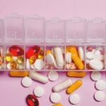 A variety of pills in a weekly pill organizer on a pink background.