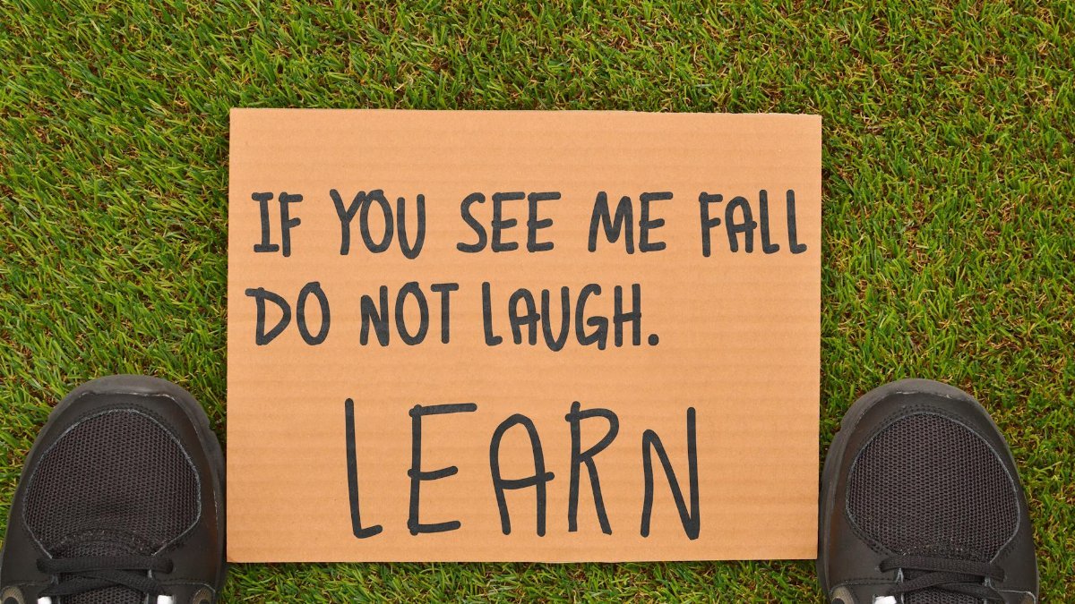 Cardboard sign with motivational message beside sneakers on green grass.