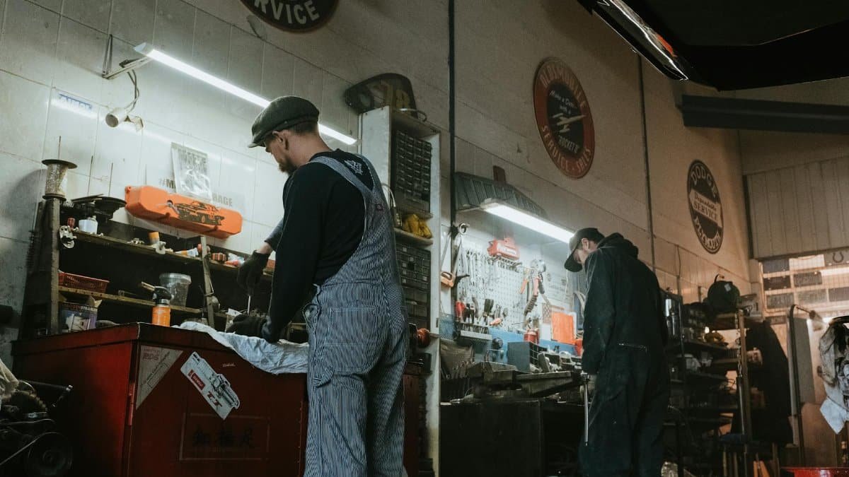 Two mechanics in a garage working on vehicle repair and maintenance.