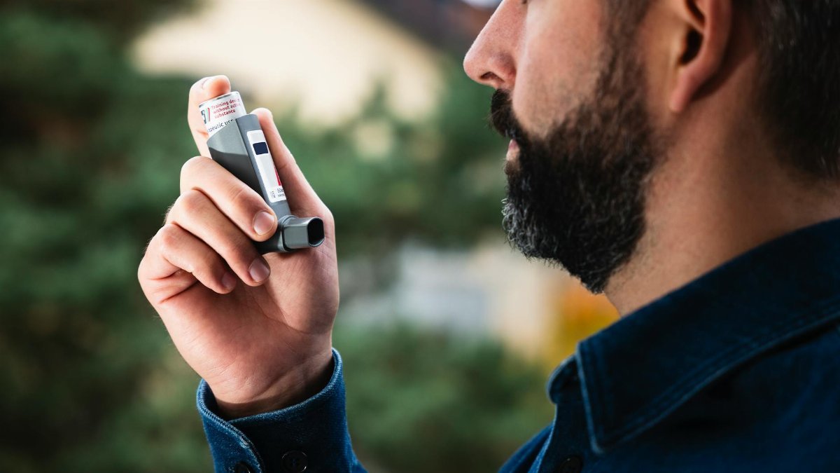 Adult man uses inhaler outdoors for asthma relief, focusing on respiratory health.