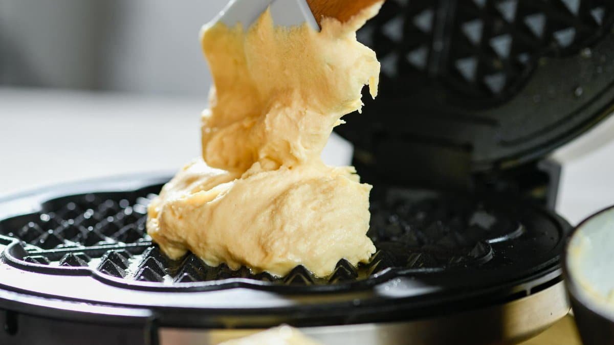 Delicious waffle batter being spread on a waffle maker for a tasty breakfast.