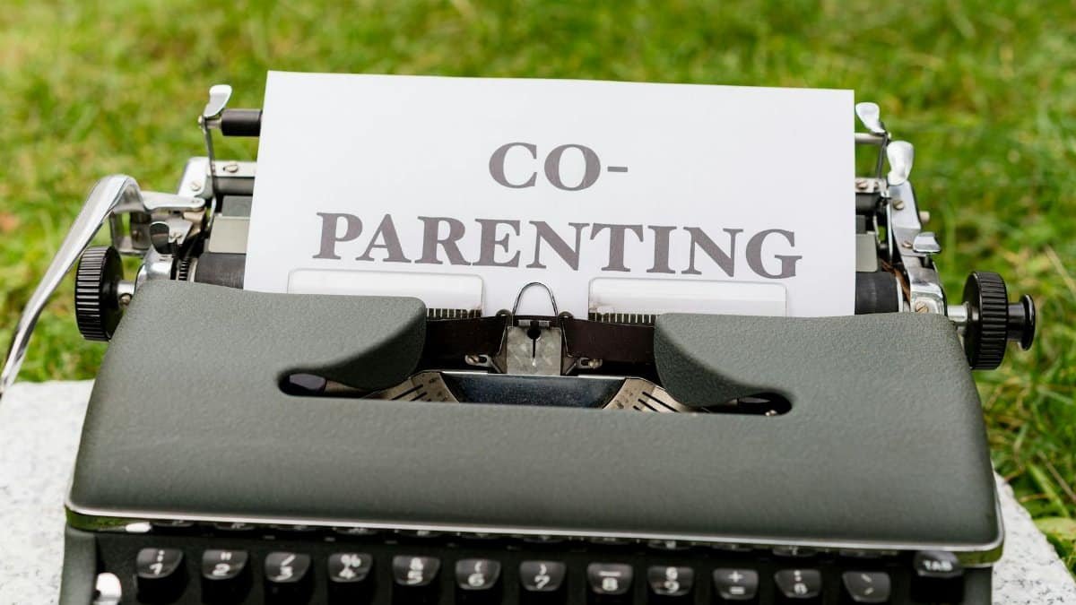 Close-up of an antique typewriter with 'Co-Parenting' paper, set outdoors on grass.