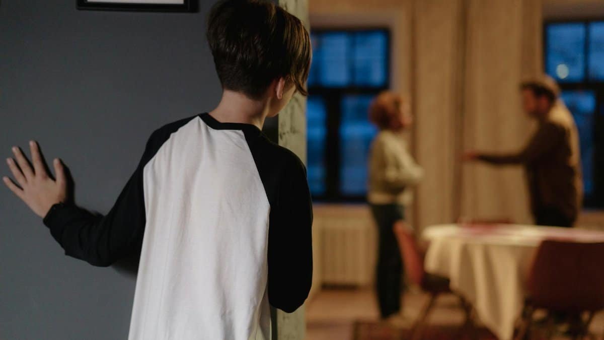 A child watches parents arguing from a doorway in a cozy home setting.