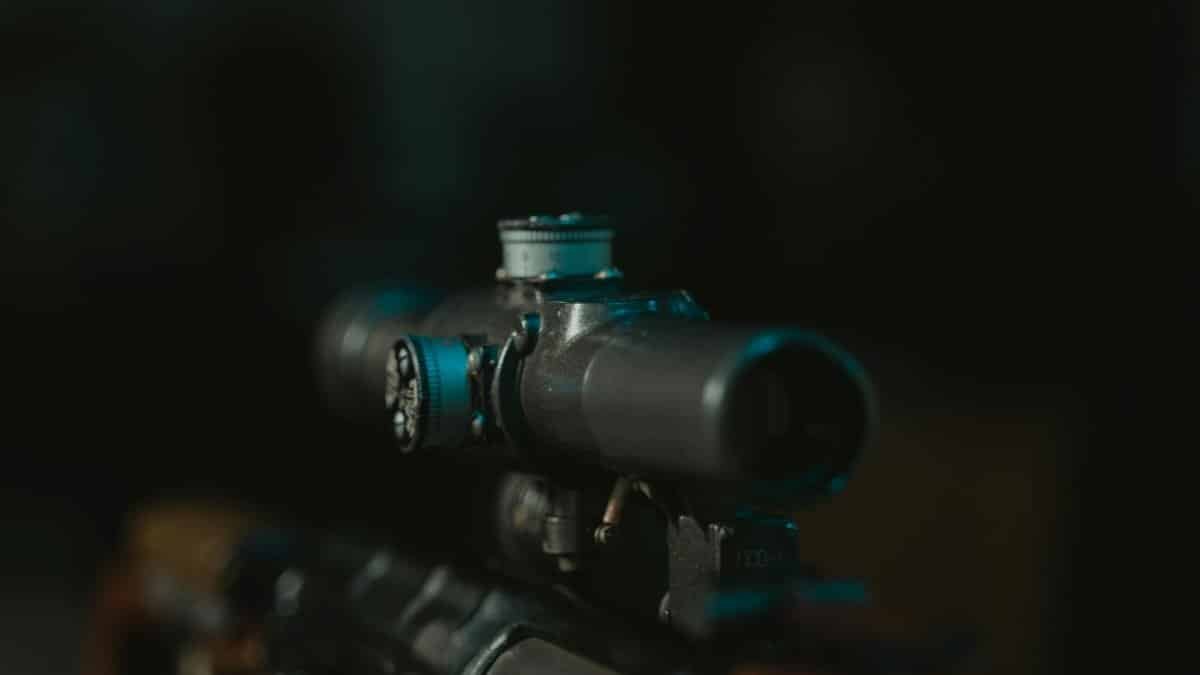 Detailed shot of a rifle scope on a firearm, in low light setting.
