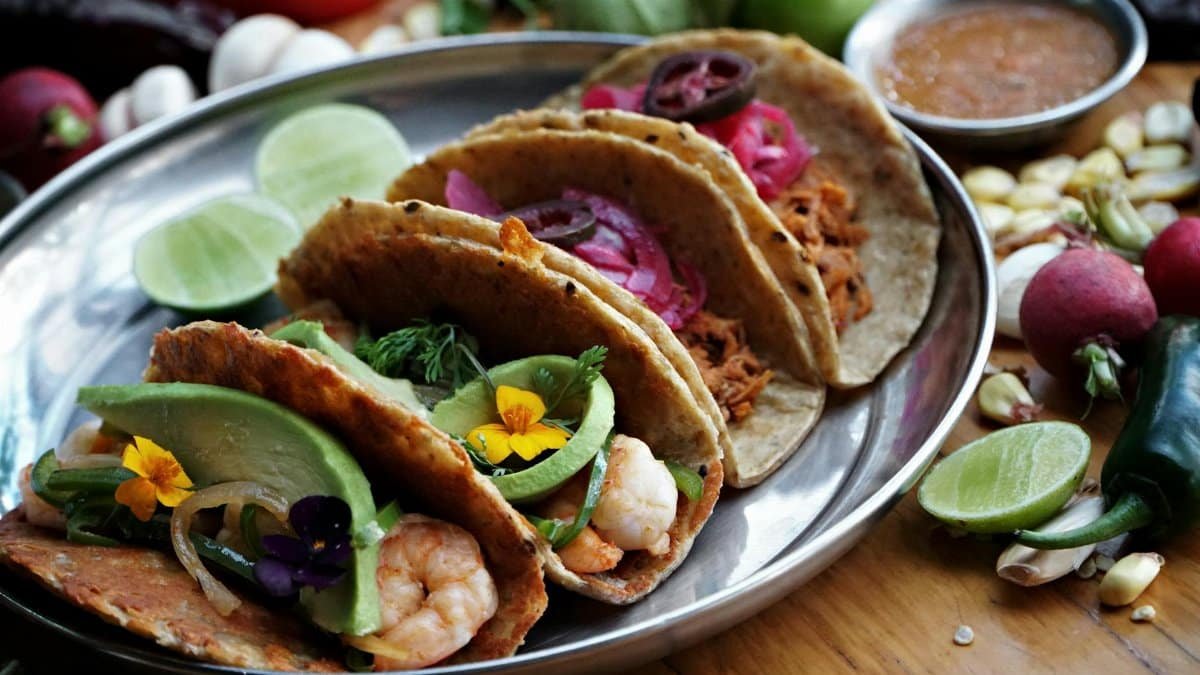 Tasty Mexican tacos filled with shrimp, avocado, and spicy sauce served on a tray.