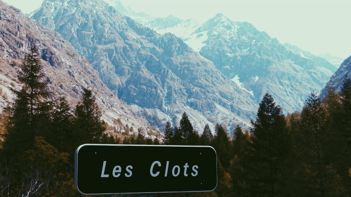 Breathtaking view of mountains and trees with a Les Clots sign in Champoléon, France.