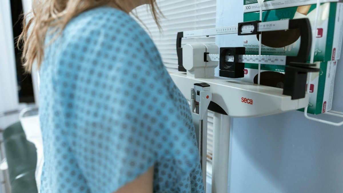 Adult female using a medical weighing scale in a healthcare setting.