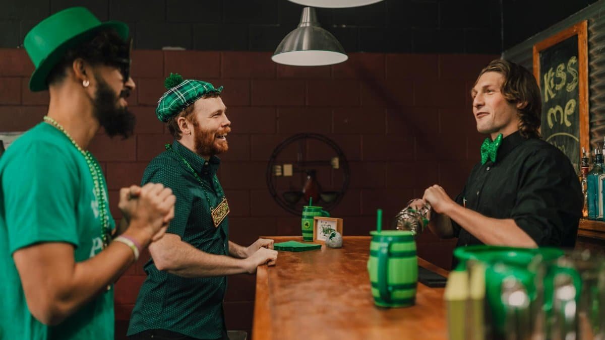 Three men celebrating St. Patrick's Day indoors at a bar wearing green attire.