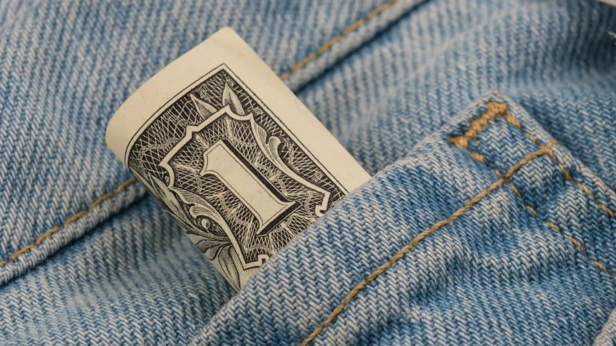 Close-up of a rolled dollar bill tucked into a denim pocket, symbolizing savings and finance.