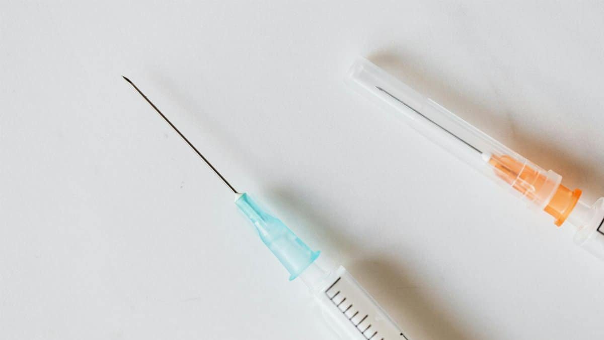 From above of medical syringe with needle placed near syringe with covered needle on white table