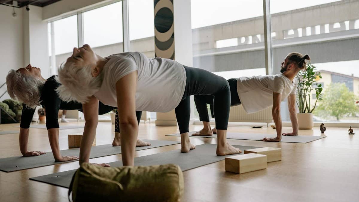 Adults practicing reverse tabletop pose in a bright modern yoga studio.