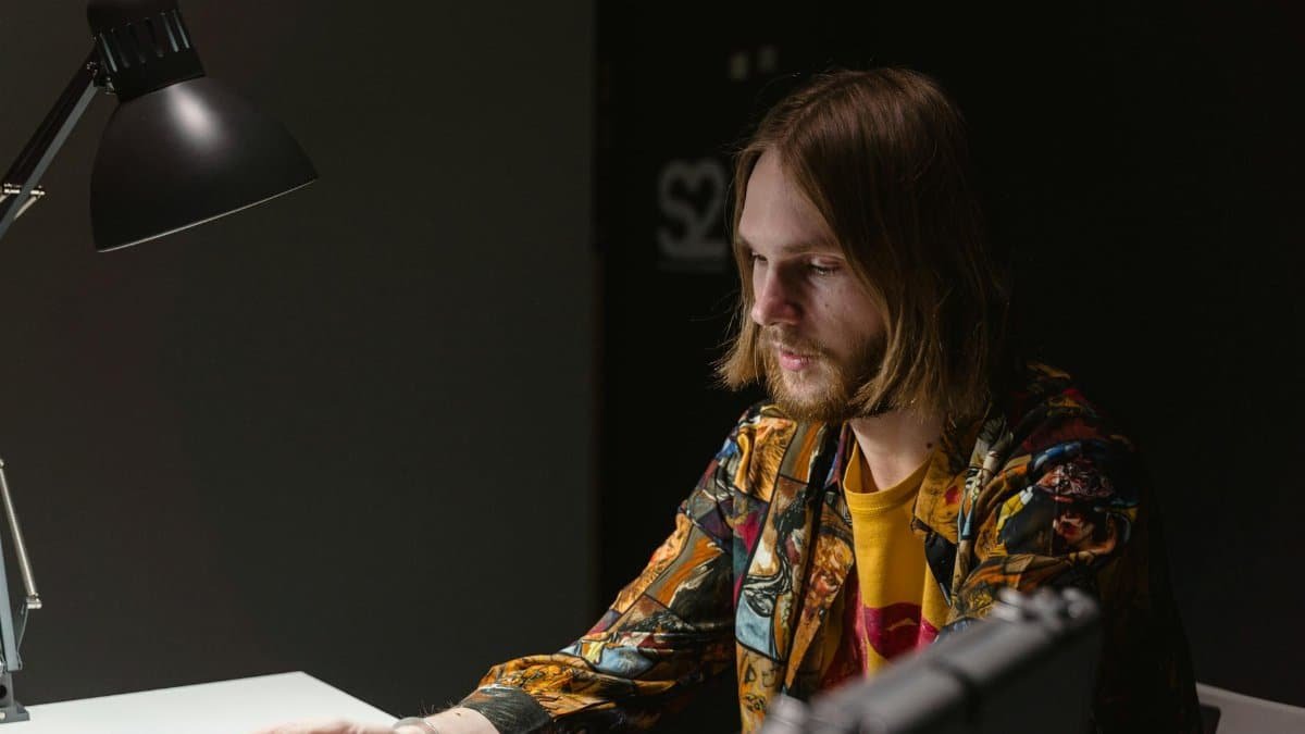 Profile of a bearded man handcuffed and sitting in a dimly lit interrogation room.