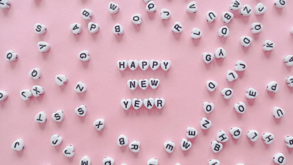 Heart-shaped letter tiles form 'Happy New Year' on a pink background. Minimalist and festive.