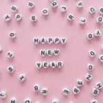 Heart-shaped letter tiles form 'Happy New Year' on a pink background. Minimalist and festive.