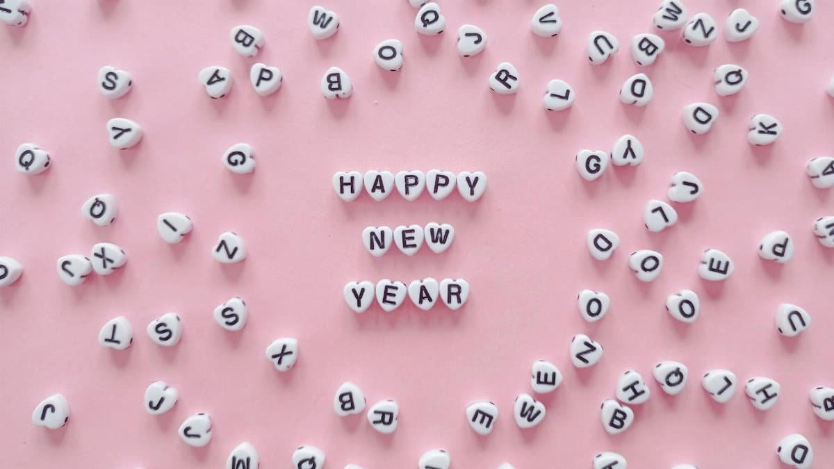 Heart-shaped letter tiles form 'Happy New Year' on a pink background. Minimalist and festive.