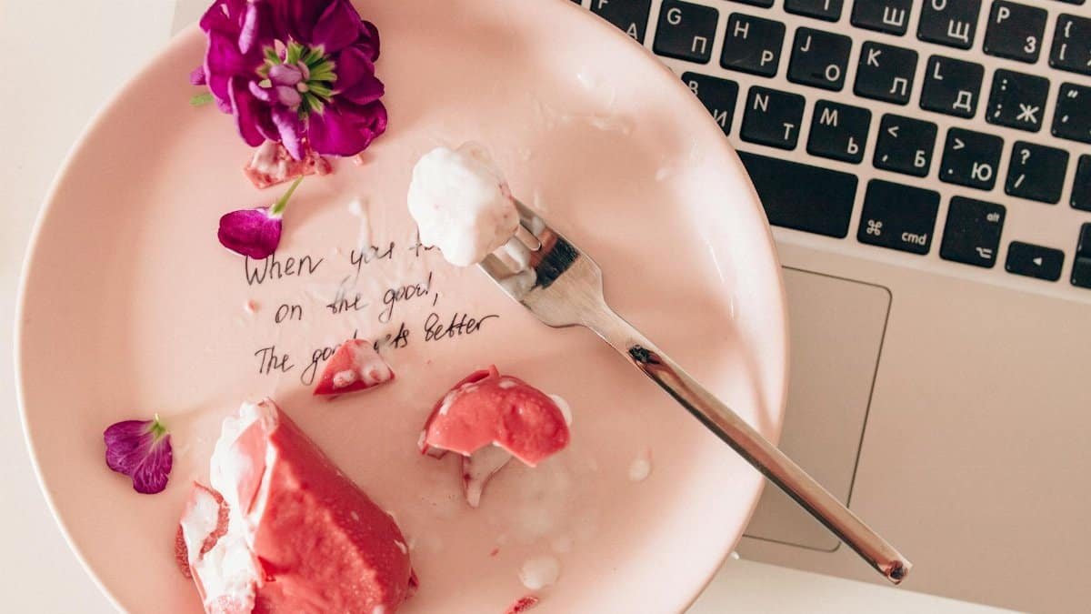 Flat lay featuring a dessert on a pink plate with an inspirational quote beside a keyboard.
