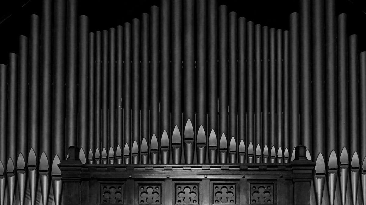 A detailed black and white photograph of a grand pipe organ's intricate design and pipes.