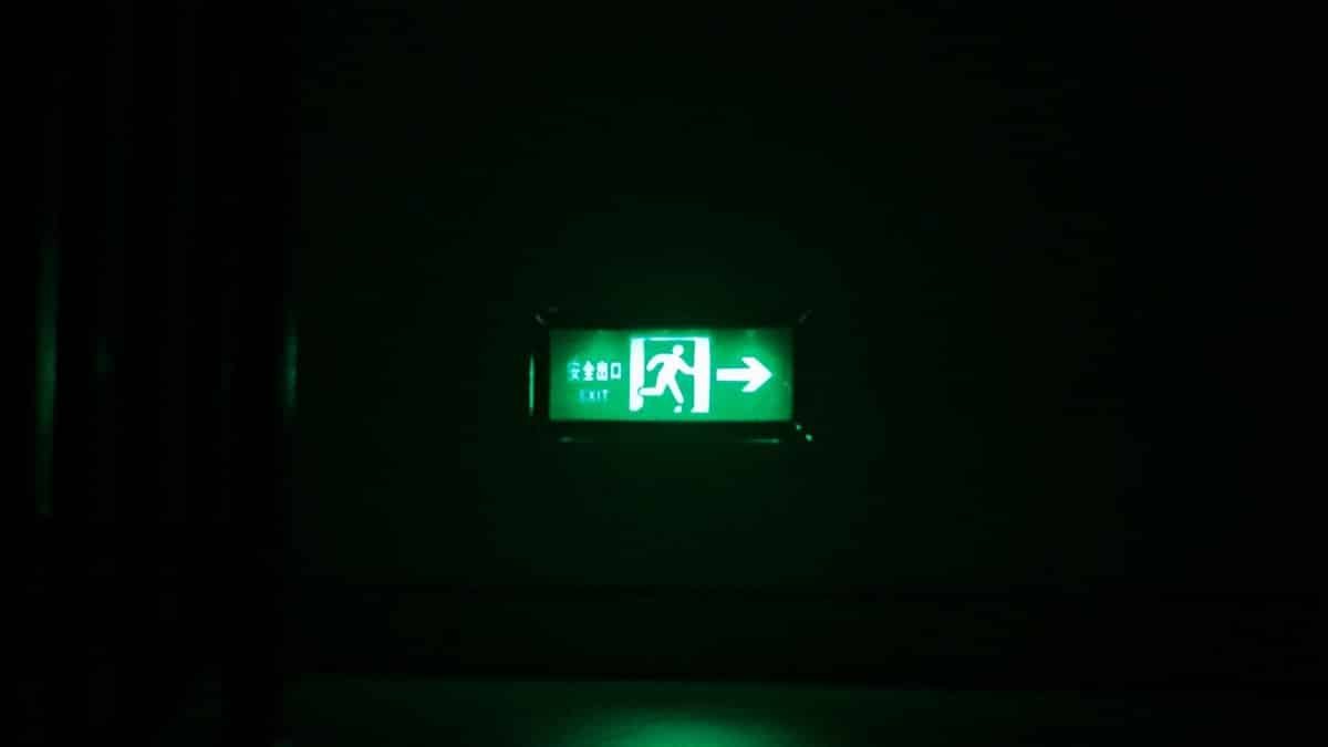 Illuminated green exit sign with directional arrow in a dark indoor setting.